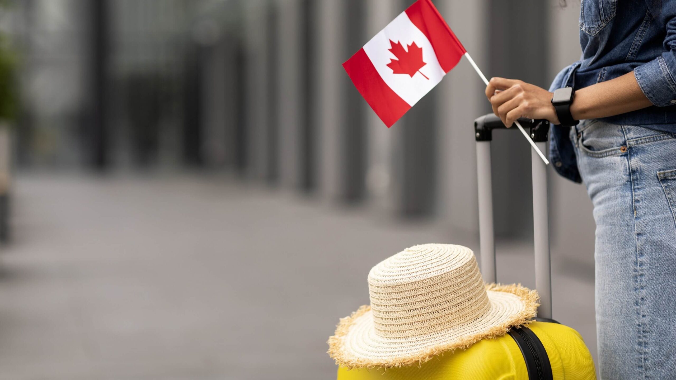 A photo f a person holding a suitcase and a Canadian flag